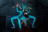 This photograph is taken inside a geodesic dome containing video and ceramic elements. A ceramic figure at the centre of the photograph has four legs, two arms, a gaping mouth in it's belly, three eyes and is bright blue in colour.