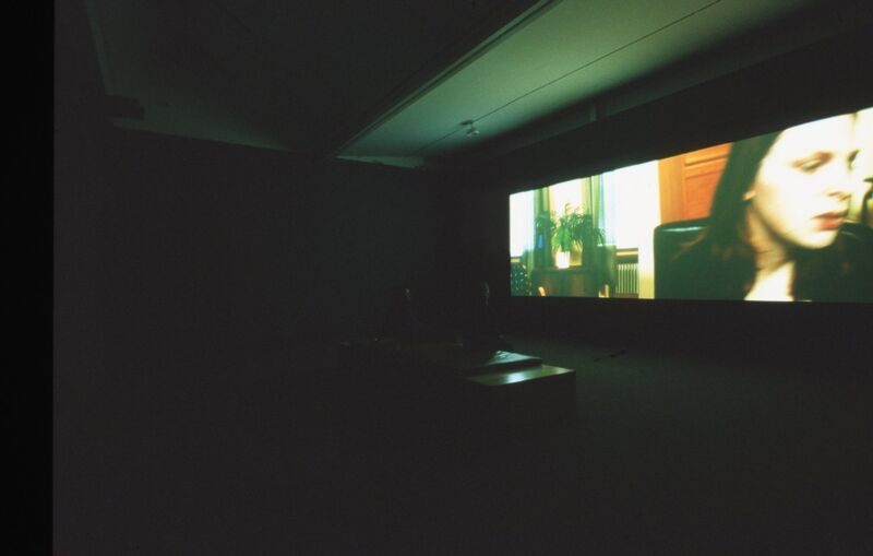 A dark gallery space with a projected film playing in it.