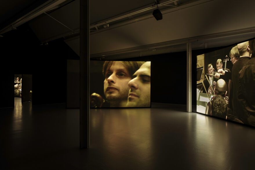 Installation documentation of gallery two, showing a two channel film projected across two big screens positioned at an angle to each other. The gallery is dark.